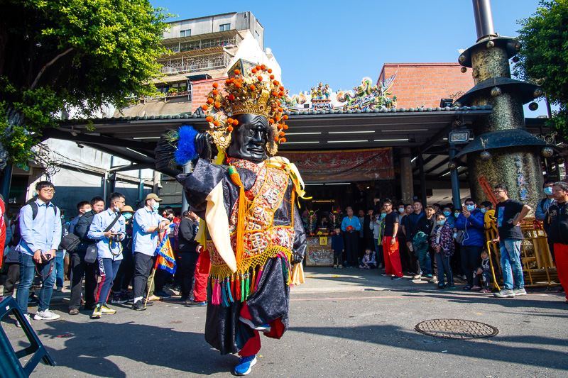 A performer dressed as a god dances in front of a temple to celebrate the temple god's birthday.