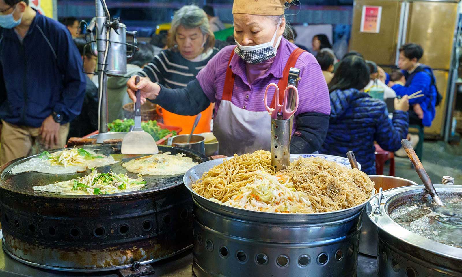 An old vender tends to multiple pots in her outdoor kitchen