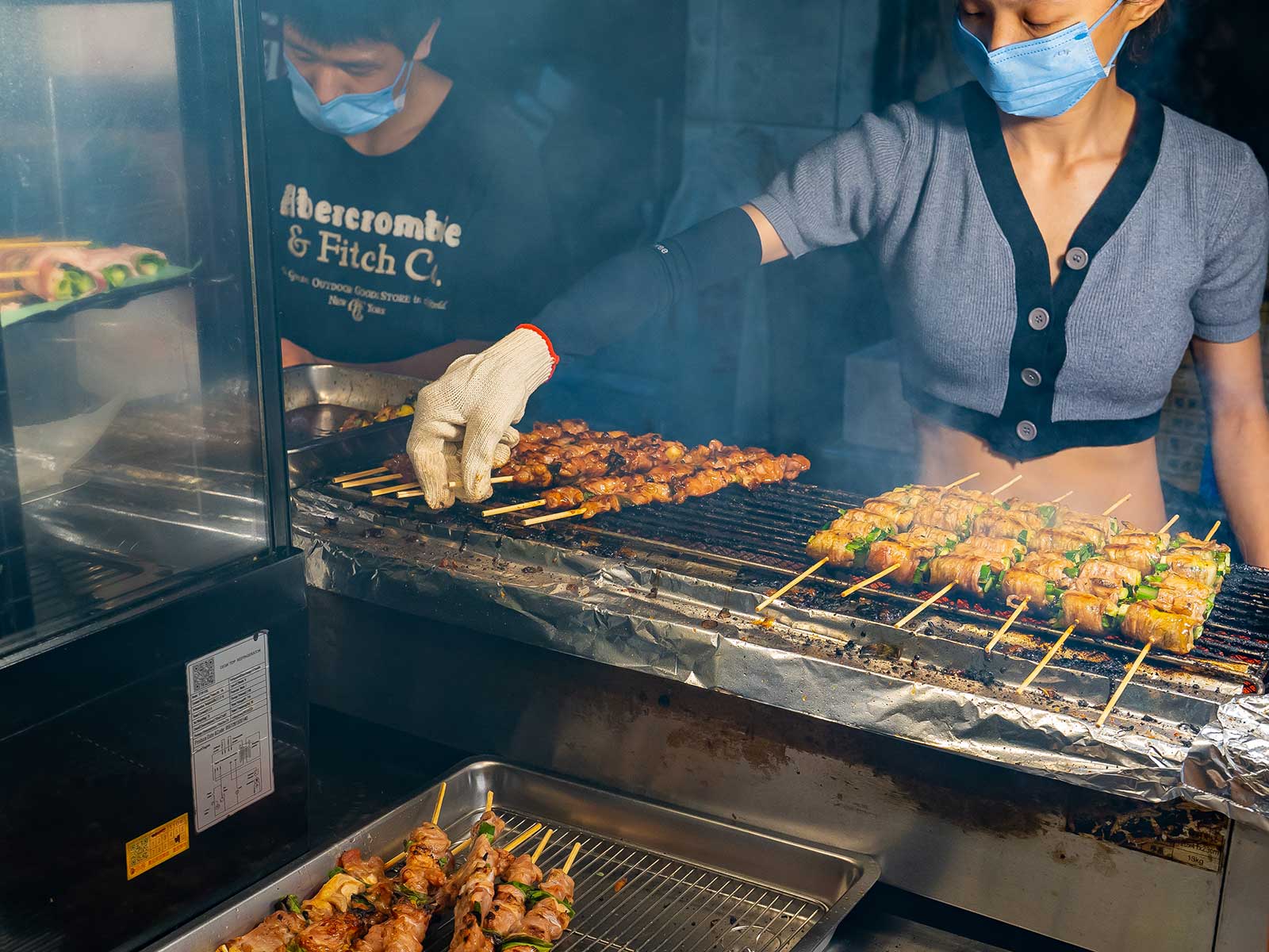 A vendor preparing grilled meat skewers.