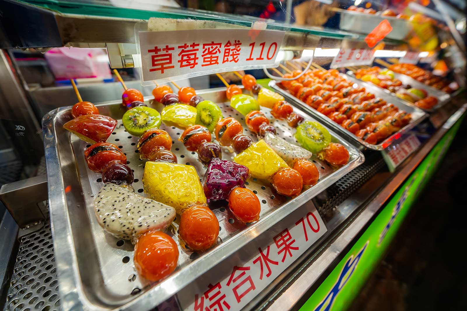 Glazed candied fruits are on display at a street food stand.