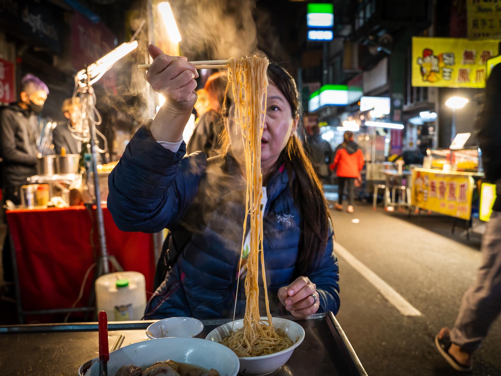 A tourist eats a bowl of noodles on the street in Keelung Night Market.
