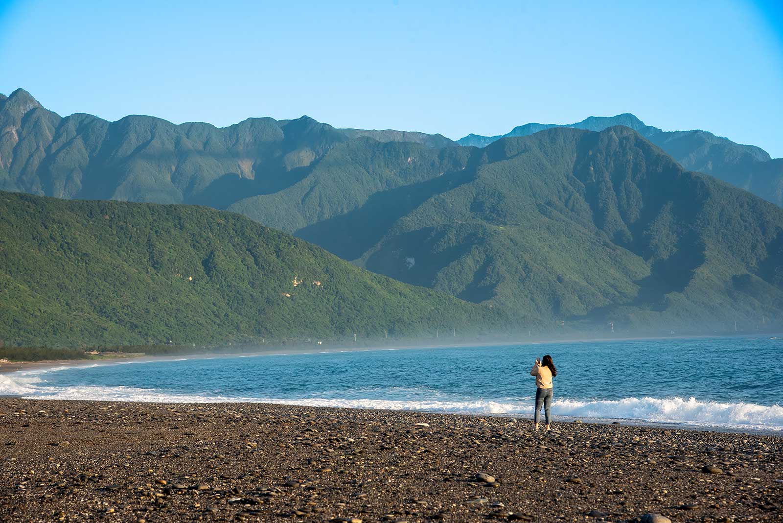 A tourist standing on Qixingtan Beach takes a photo of the nearby mountains.