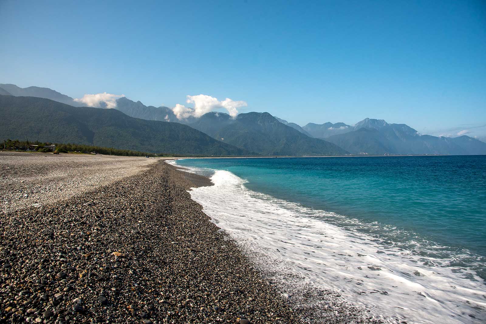 A wave crashes down on the rocky shore of Qixingtan Beach as the mountains of Taroko National Park are visible in the background.