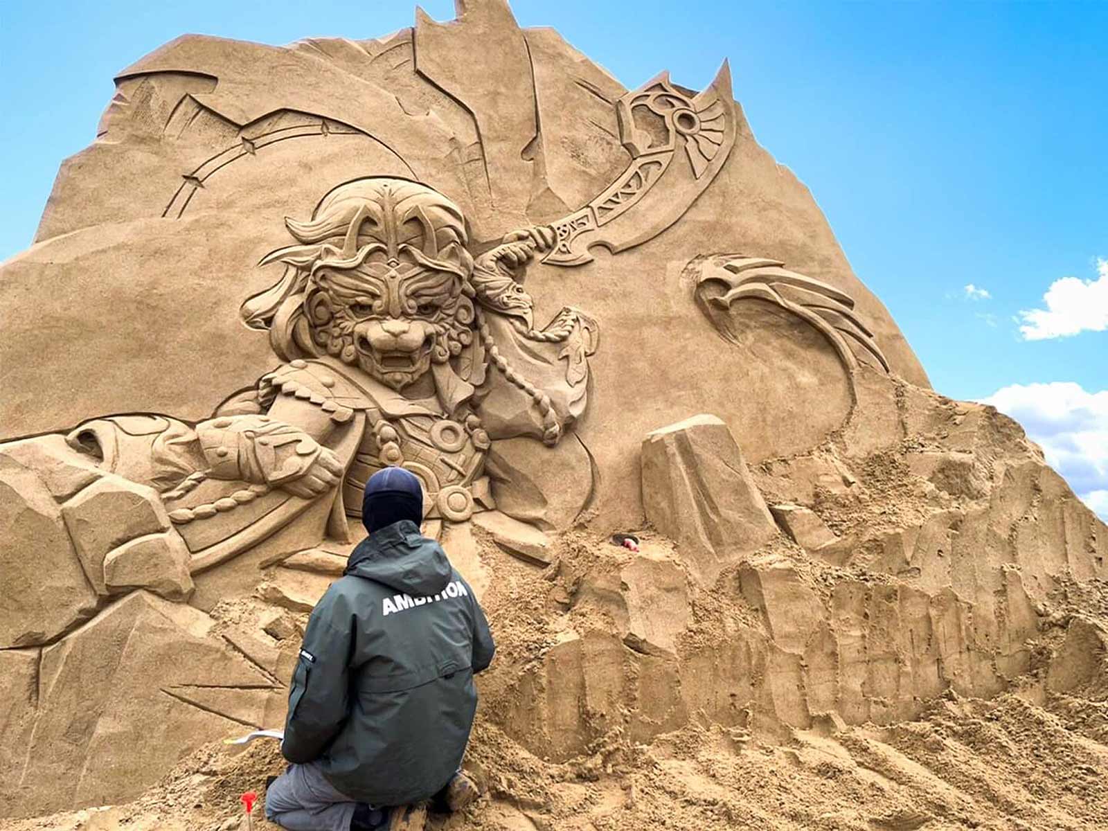 An artist working on carving his sand sculpture; the sculpture stands 3 to 4 meters tall.