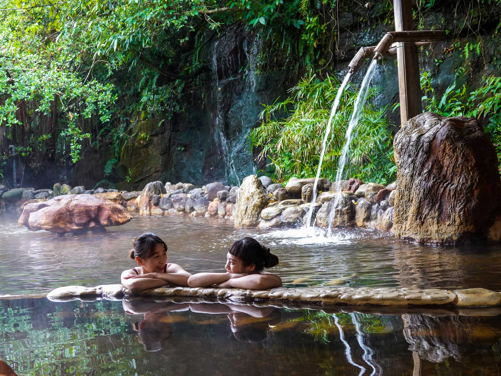 Bathers enjoy a natural-looking hot spring pool made with cement, rocks, and bamboo