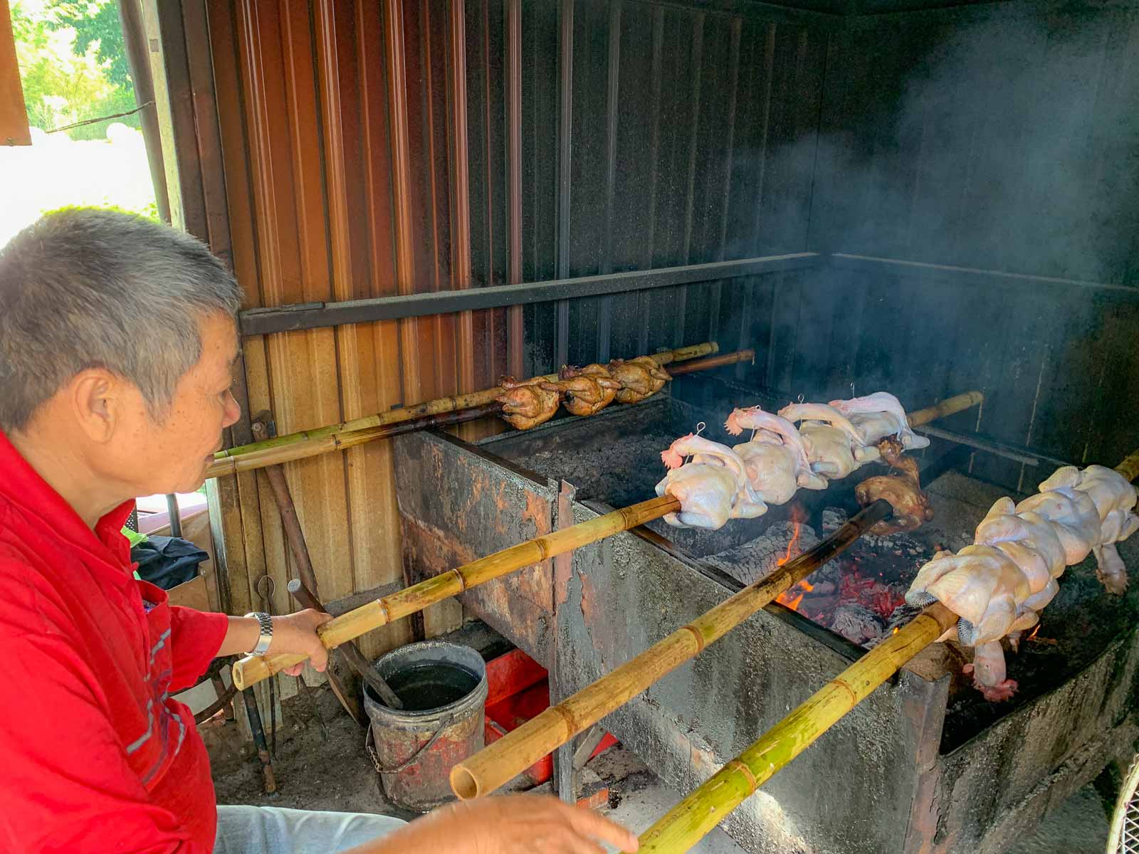 Chickens, mounted onto bamboo, are roasted over an open fire.