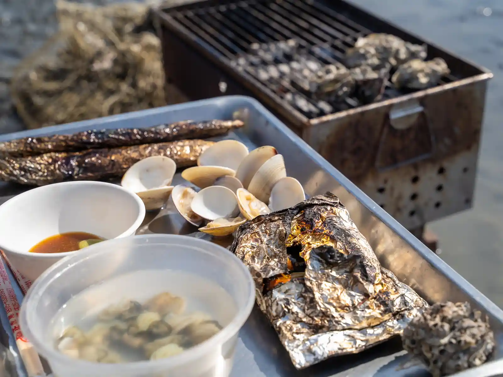 Clams, sauces, and other food wrapped in tinfoil is being heated on a grill.