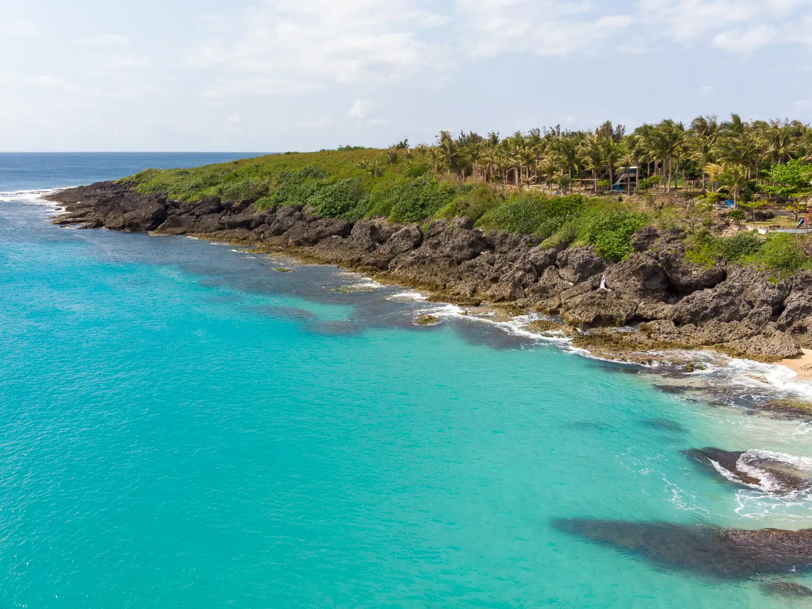 Volcanic rocks and small bluffs are visible at the northern end of the Baishawan Beach.