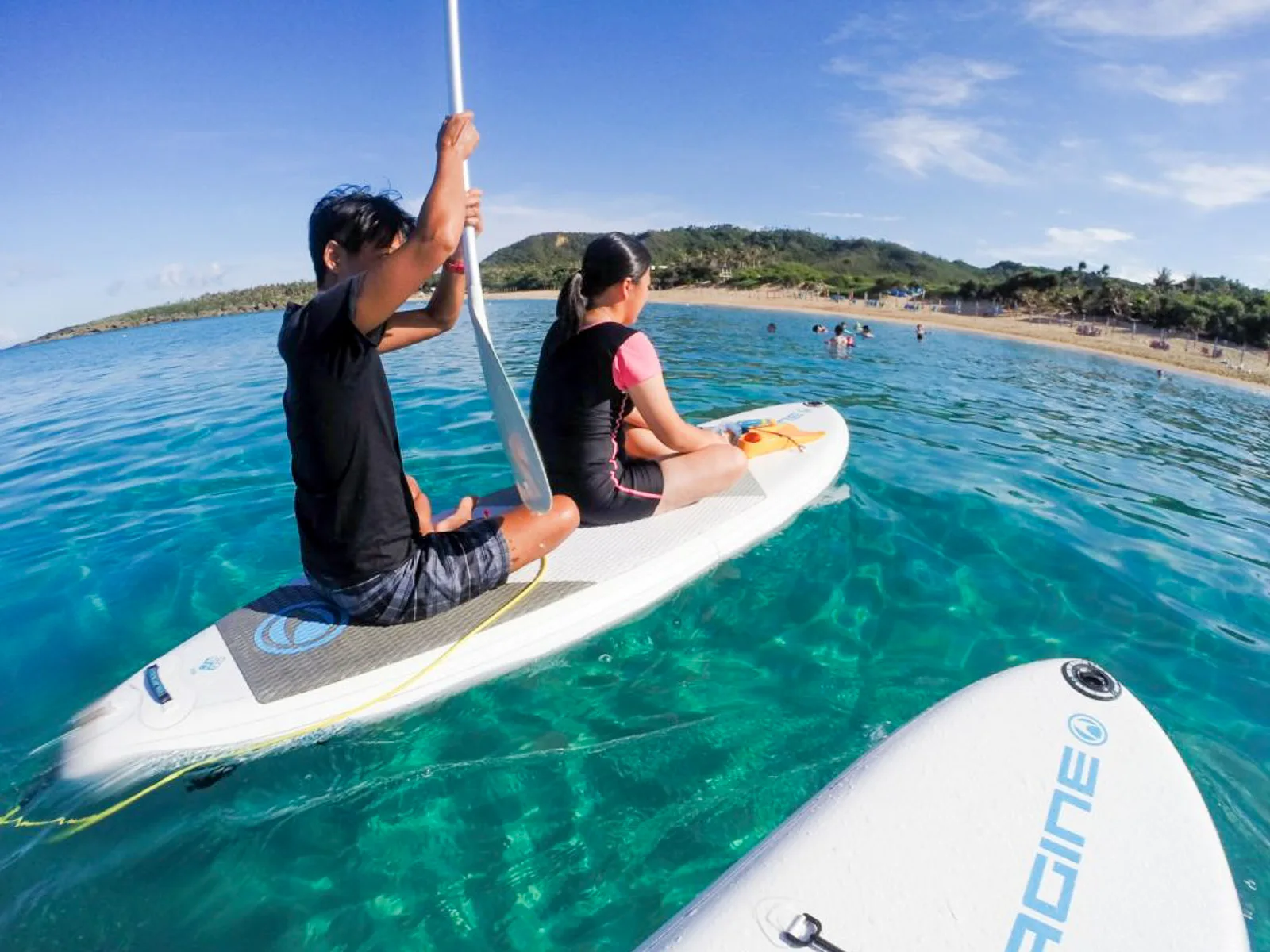 Two paddleboarders paddle offshore.