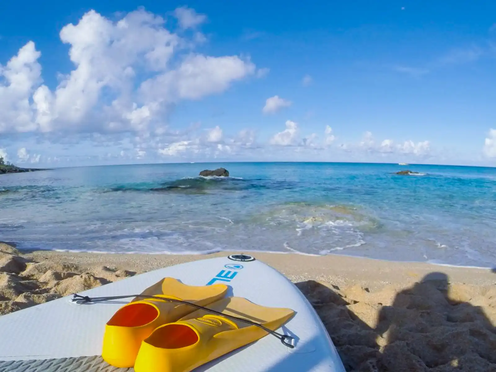 A paddleboard and fins on golden sand.