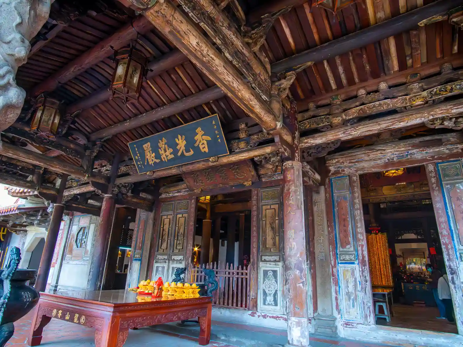 An offering table sits in front of the entrance to the main hall, which is decorated with many hand-painted wooden panels.