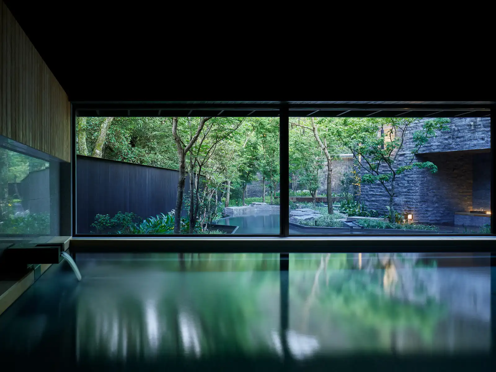 The water in a large indoor bathing pool is perfectly still and the garden can be seen through floor-to-ceiling windows.
