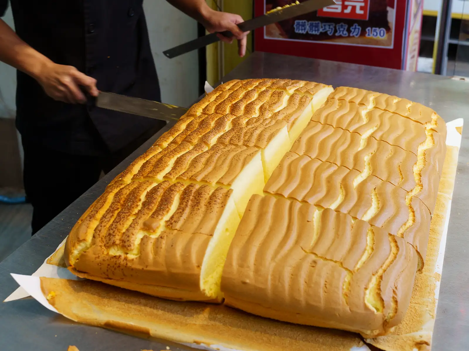 A large loaf of castella cake being cut into portions.