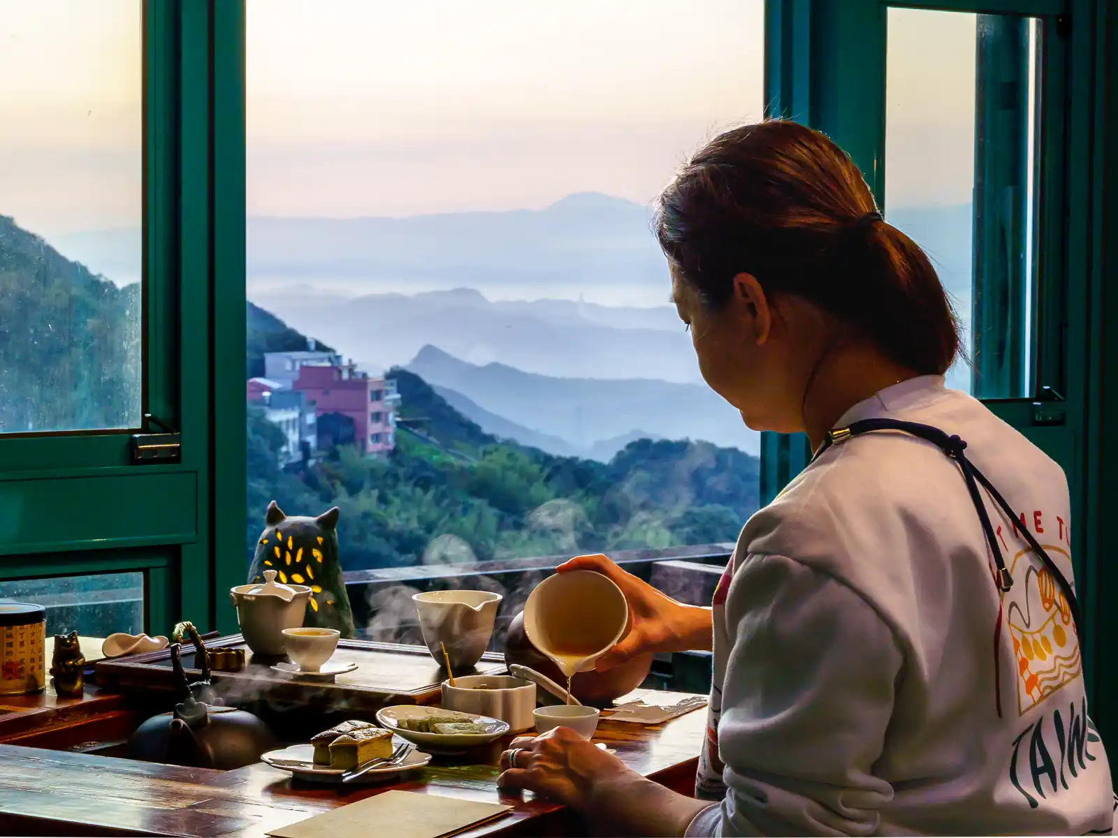 Tea is being brewed in front of a landscape of foggy mountains.
