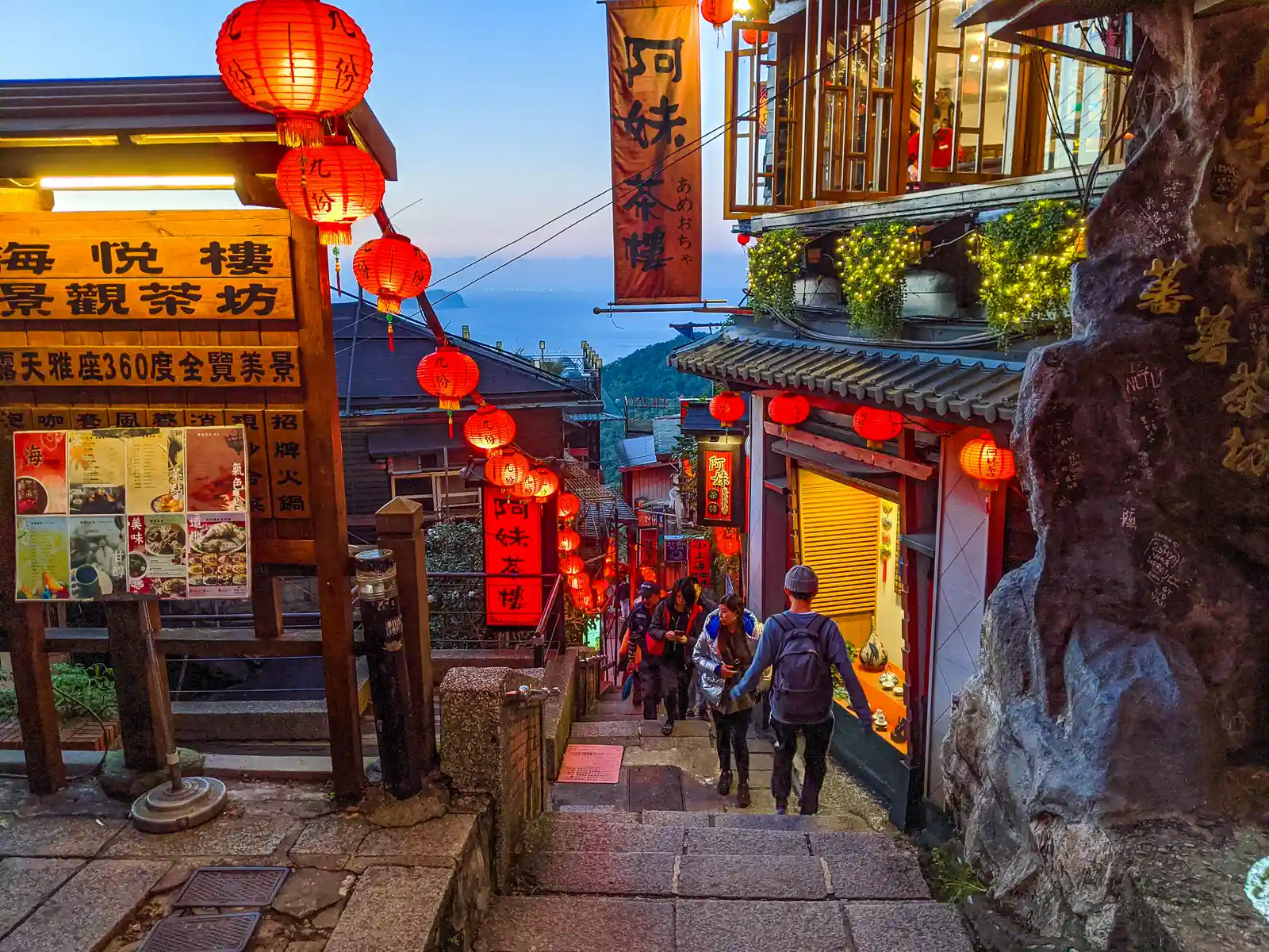 Looking down the lantern-illuminated Shuqi Road, the adjacent hills and pacific ocean appear below, while the Amei Tea Houses overlooks the road.