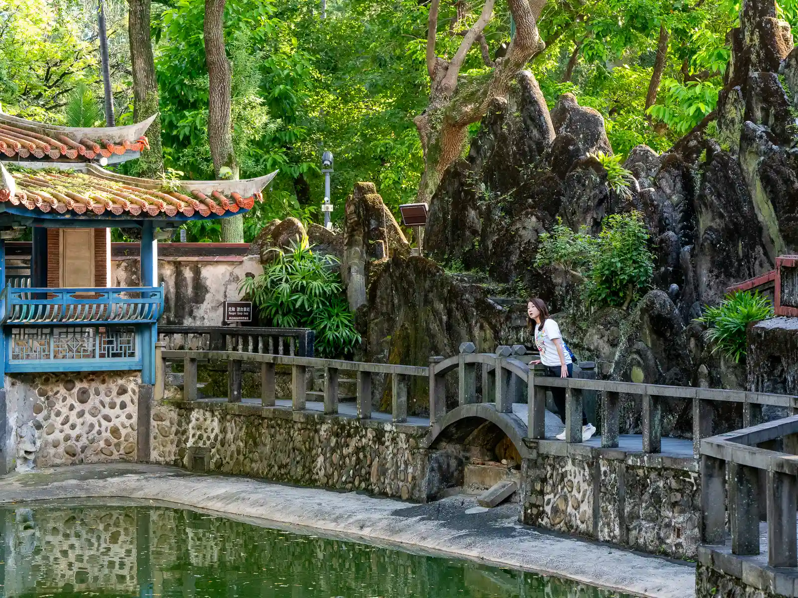 A pond in the garden is bordered by a stone bridge and walkway.