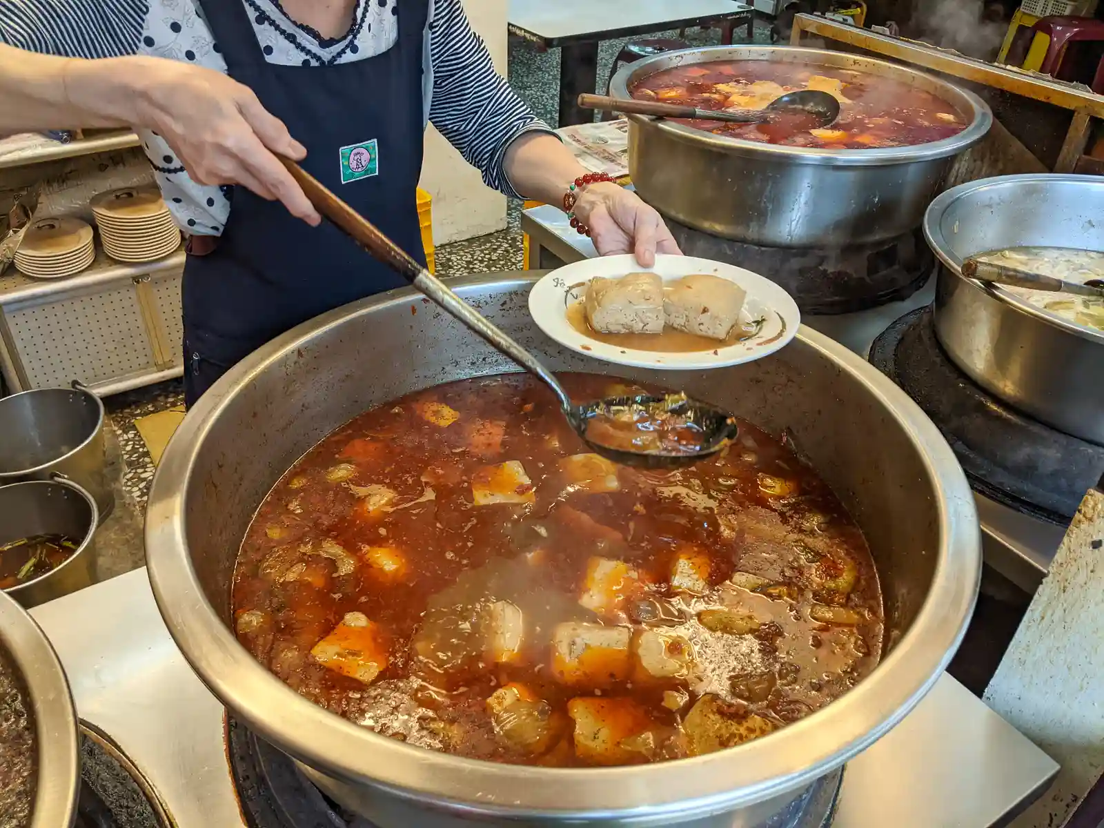 Several pieces of braised tofu are being served out of Tofu out of an industrial sized pot.