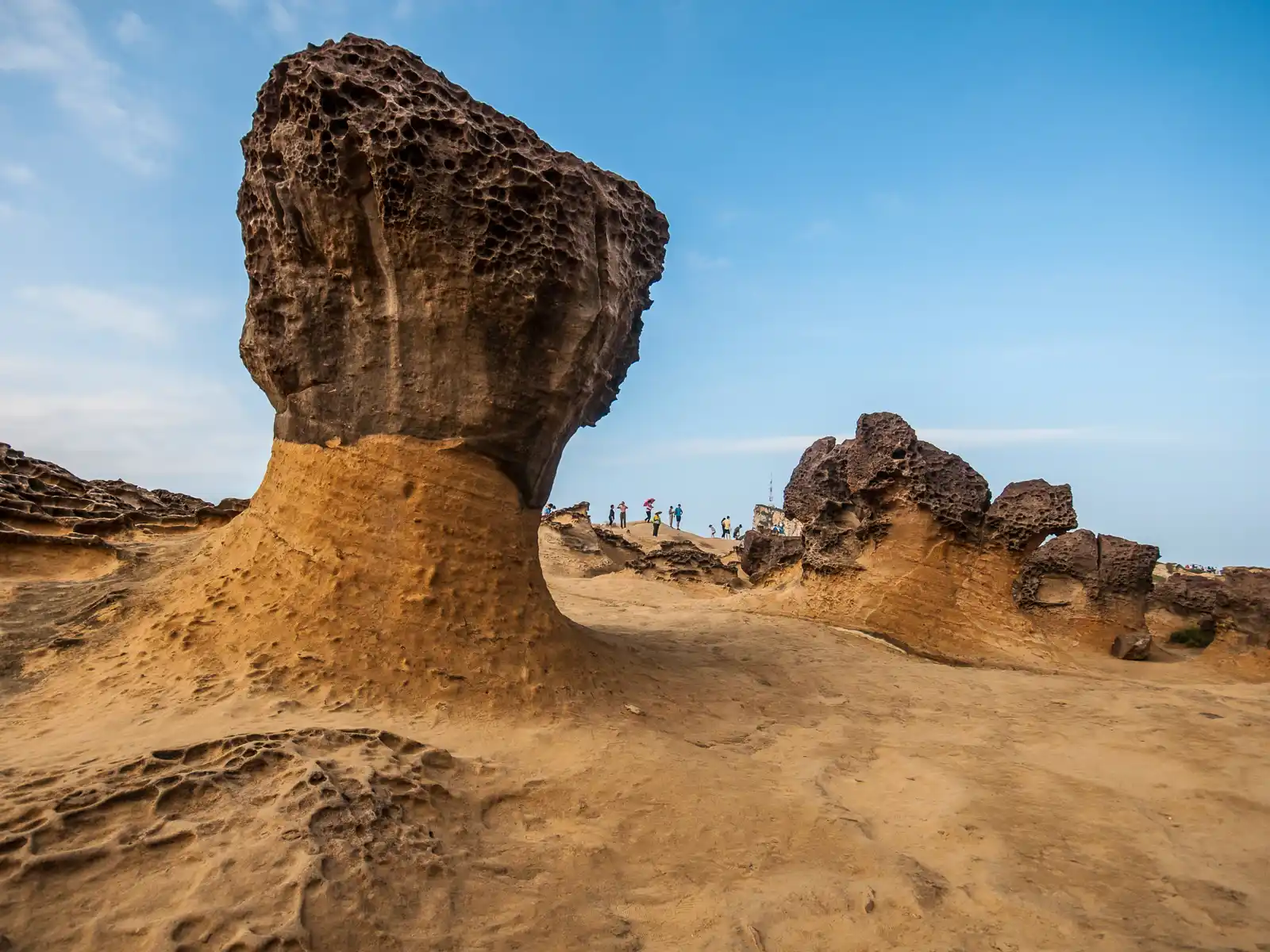 A tofu-shaped rock that features honeycomb erosion is perched over smooth sandstone.