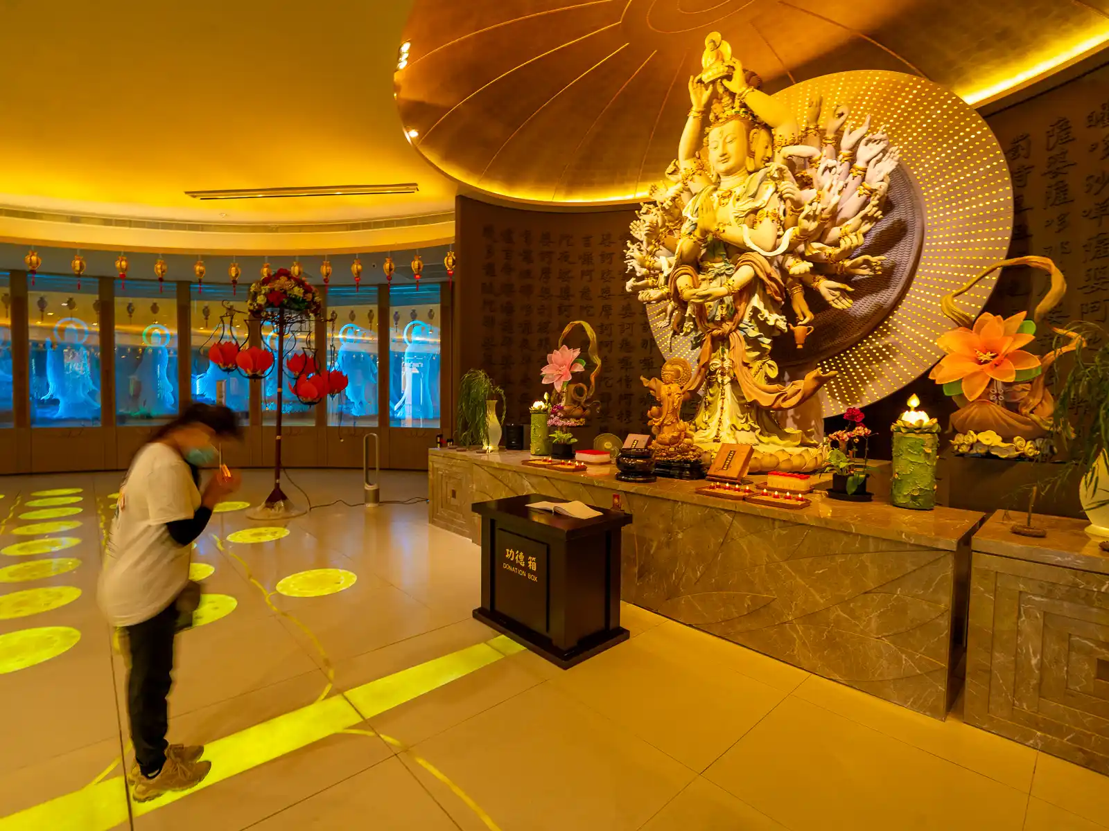 A tourist bows down before the Thousand-Armed, Thousand-Eyed Avalokitesvara Bodhisattva statue in a circular room.