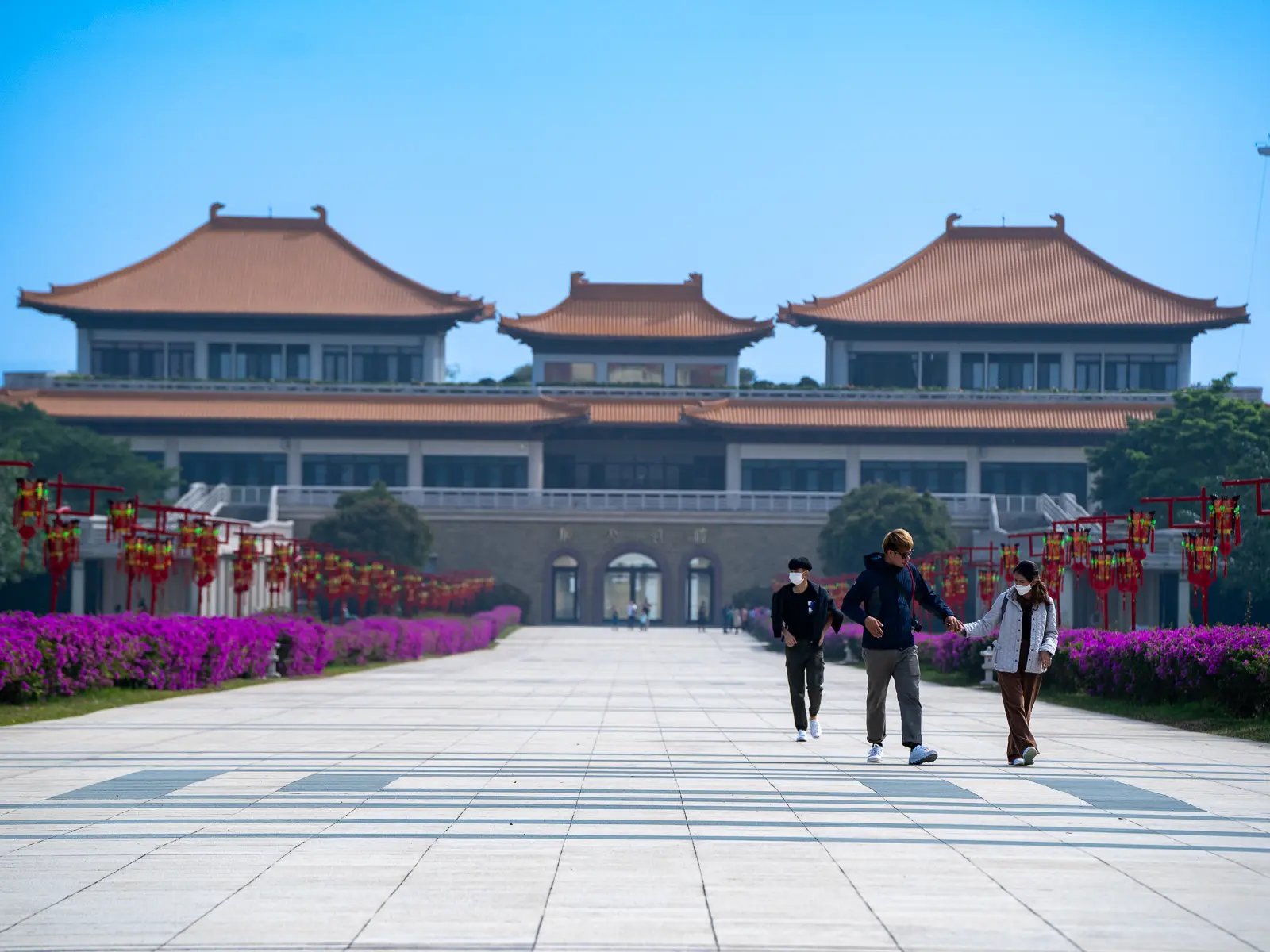 Tourists walk along a broad stone walkway and through neatly maintained gardens.