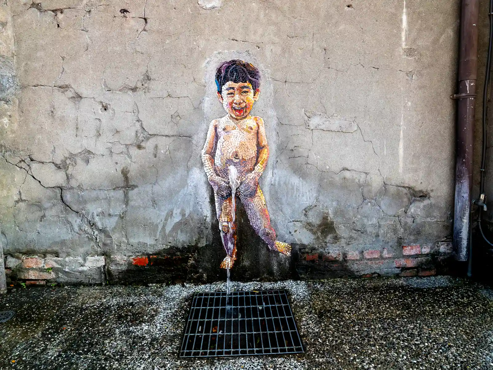 A mural of a little boy urinating is painted just above a sewer grate.