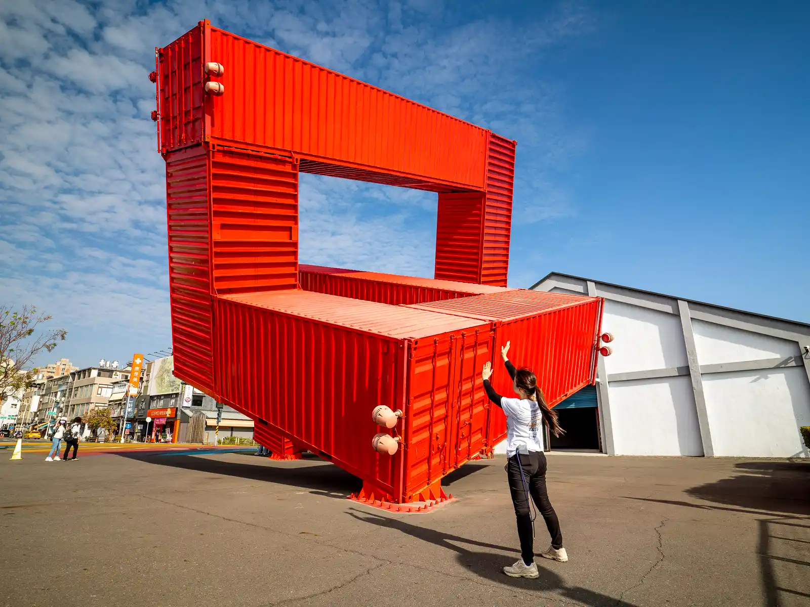 A tourist poses with a large piece of installation art made from repurposed cargo containers.