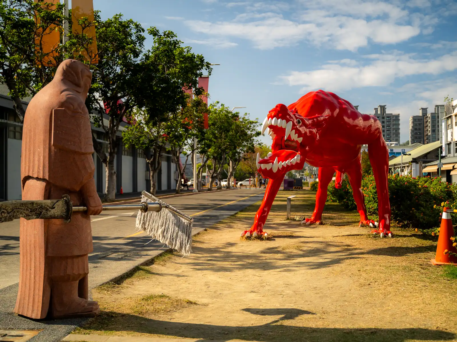 A statue of a monk or farmer with a mop faces a statue of a tall red dog-like creature.