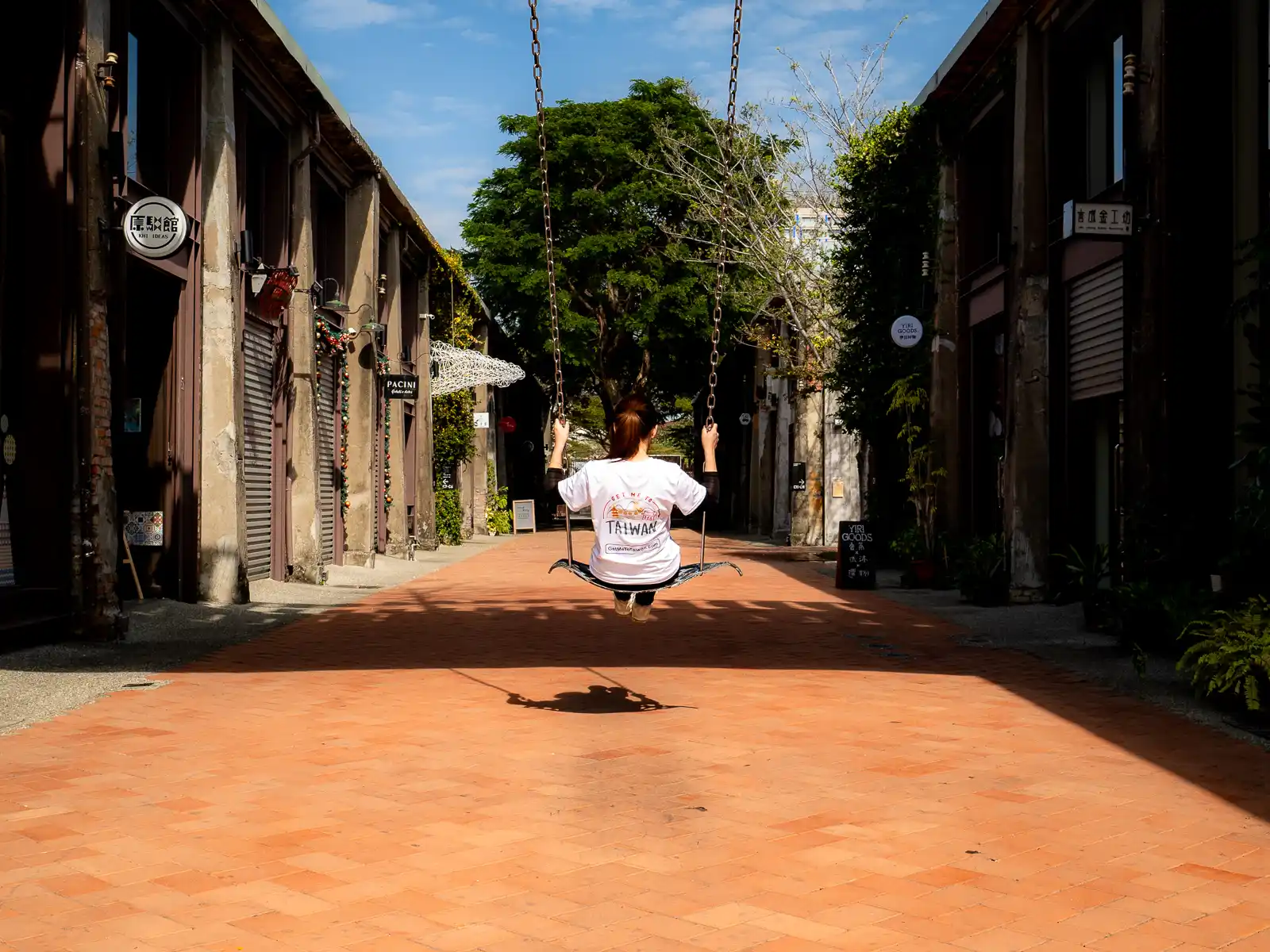 A tourist swings on a swing suspended between two warehouses.