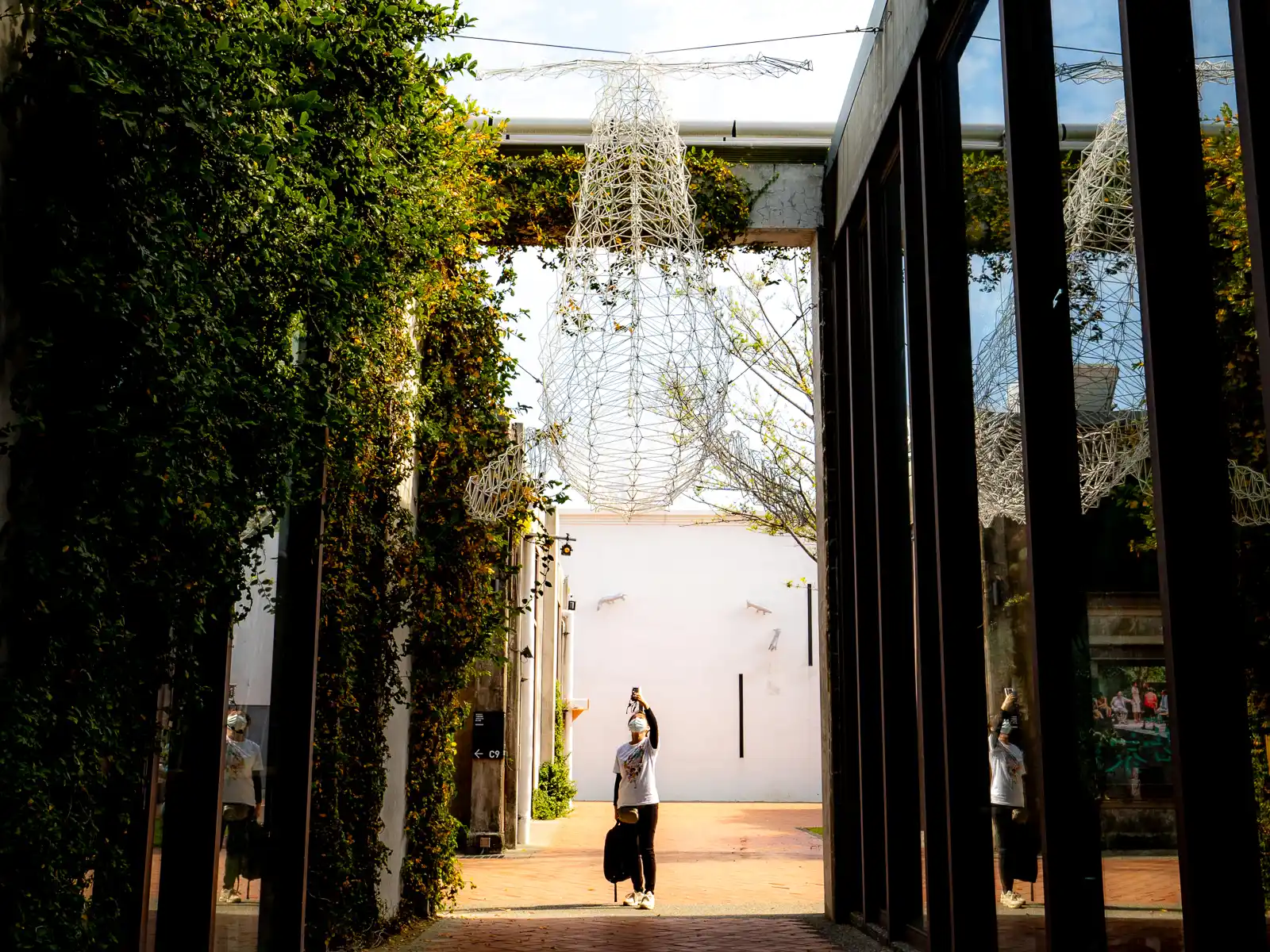 A wireframe sculpture is suspended between two buildings,