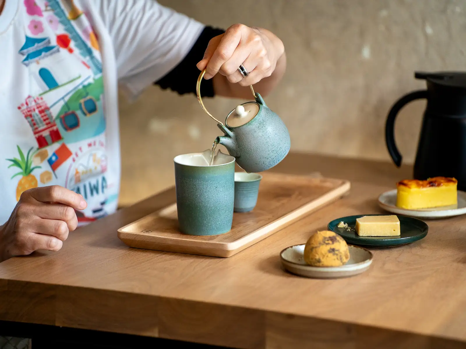 Tea is poured from a beautiful sea green teapot into a tea pitcher.