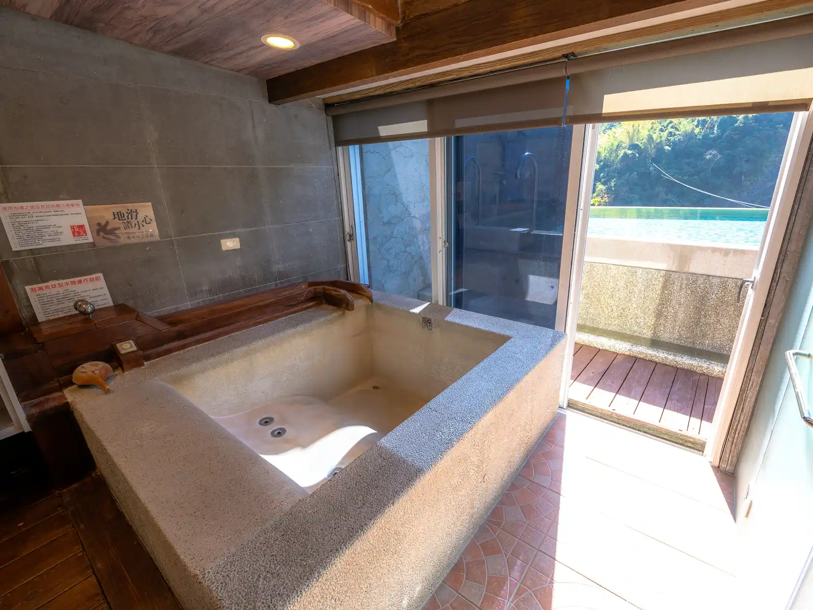 A sculpted indoor hot spring tub with jets looks out on a balcony and nature outside.