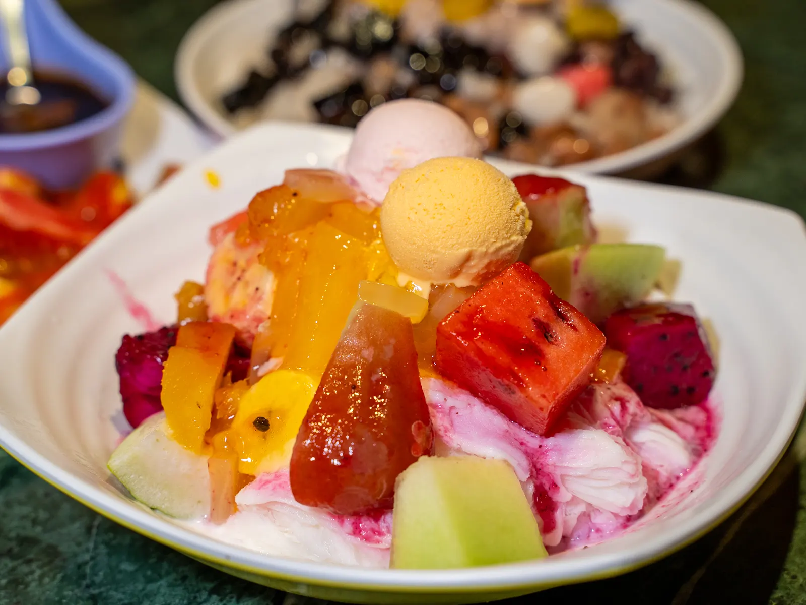 A bowl of shaved snow is topped with ice cream and fresh fruit.