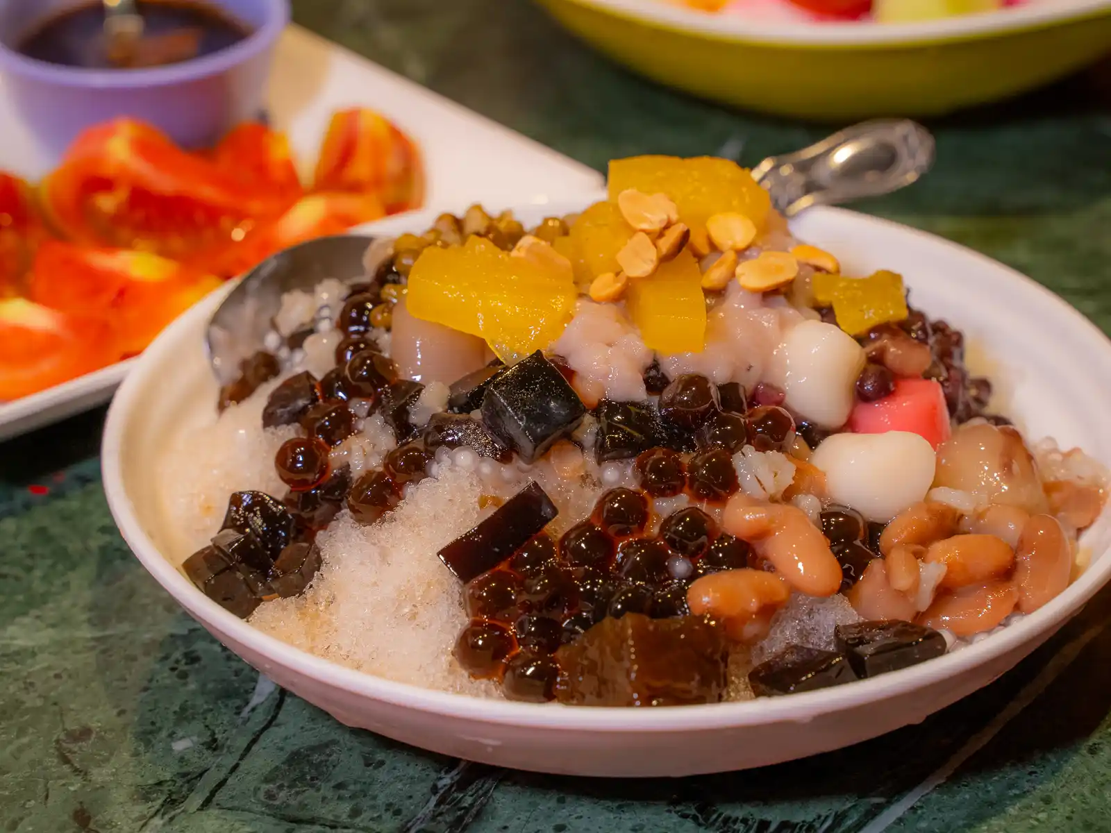 A bowl of shaved ice is topped with traditional toppings including peanuts, kidney beans, and tapioca pearls.