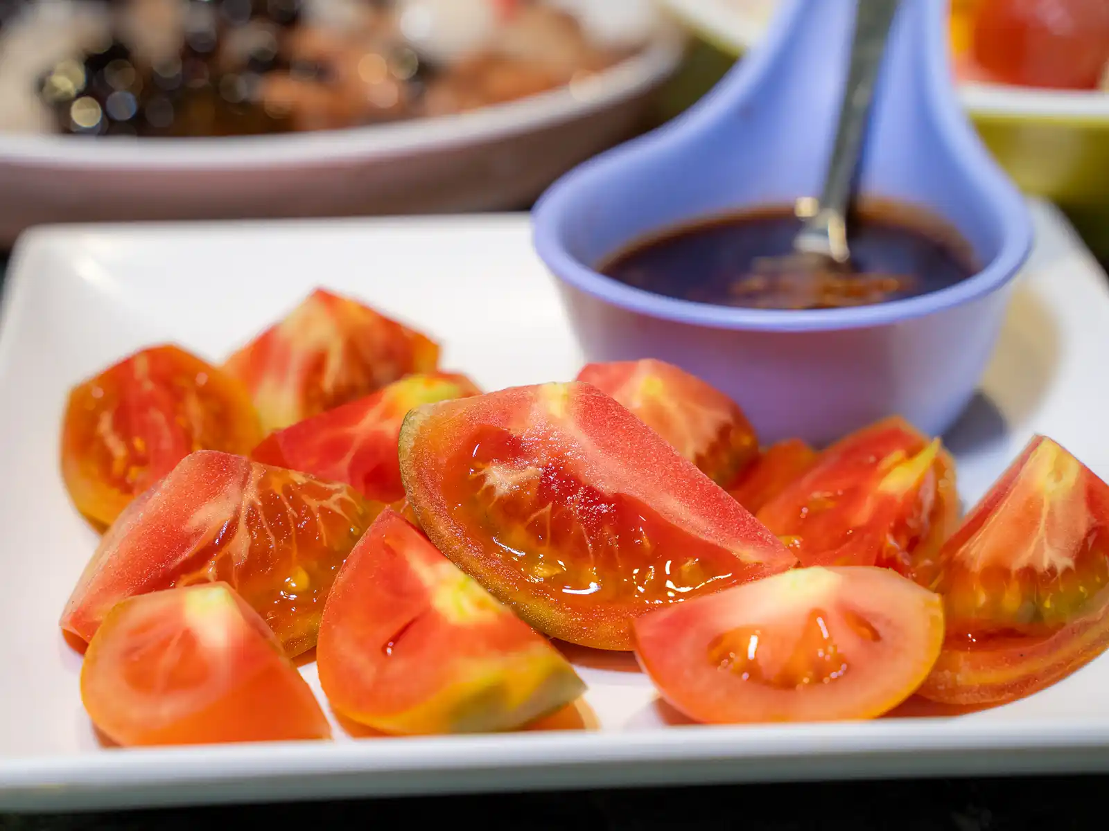 A plate of sliced tomato and dipping sauce.