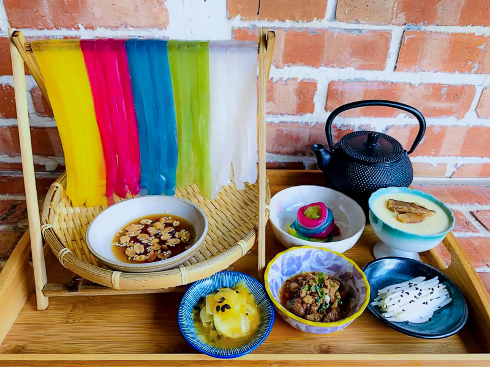 A tray features a set meal of rainbow noodles, ground pork, steamed egg, a passion fruit-based dessert, and more.