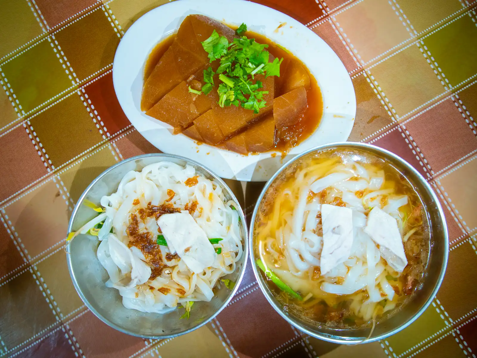 Two bowls of bantiao, one immersed in soup, and a serving of marinated radish.
