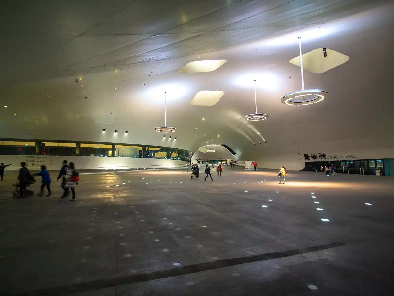 People walk through a large interior plaza with a high curved flowing ceiling.