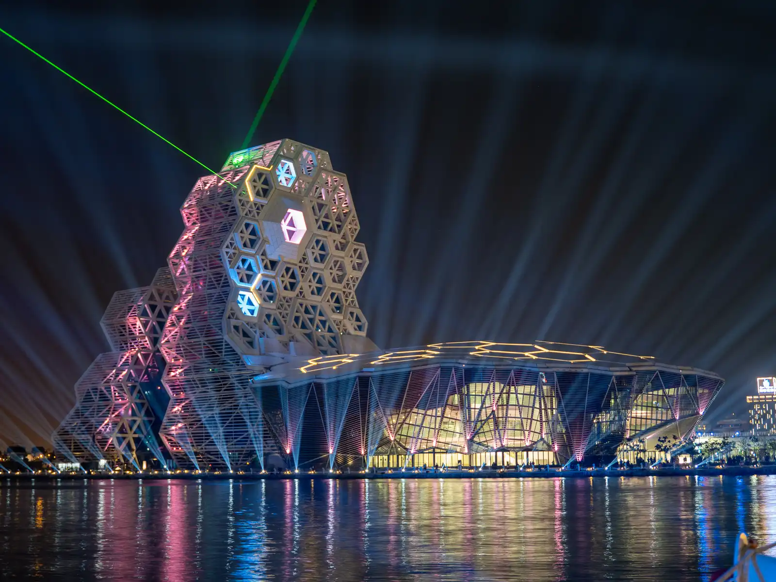 The Kaohsiung Music Center seen from across the water during a laser light show that pierces through the sky.