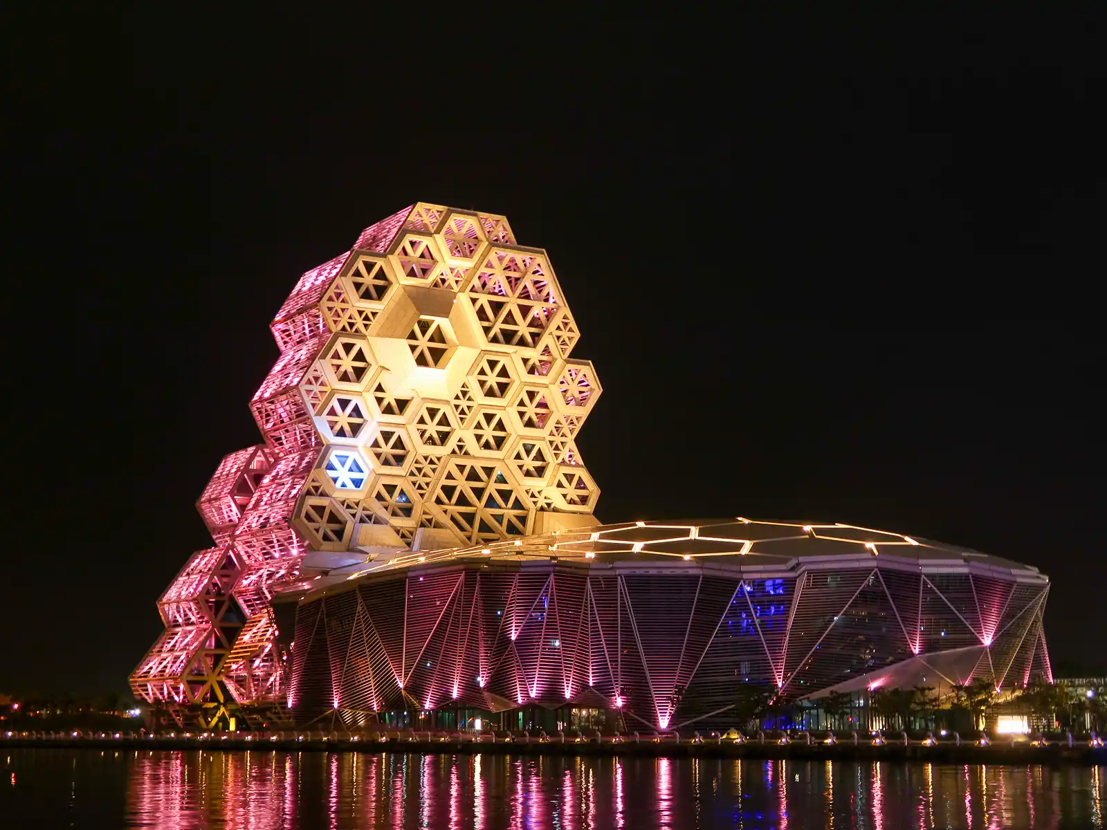 The Kaohsiung Music Center seen from across the water with its exterior illuminated at night.