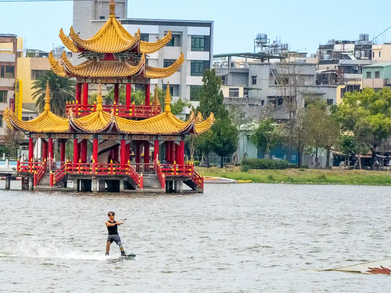 A wakeboarder rides in front of one of the floating temples of Lotus Pond.