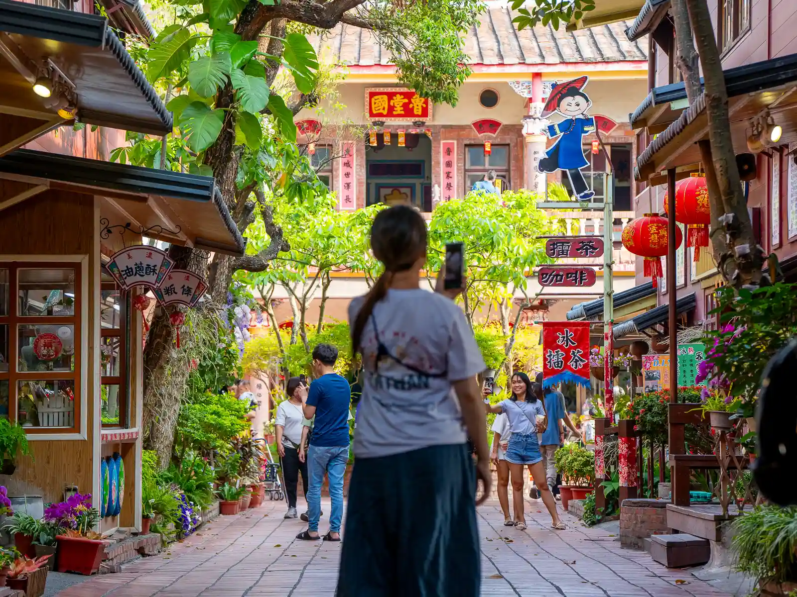 A tourist takes a photo of the shops on Meinong Folk Villages lush main walkway.
