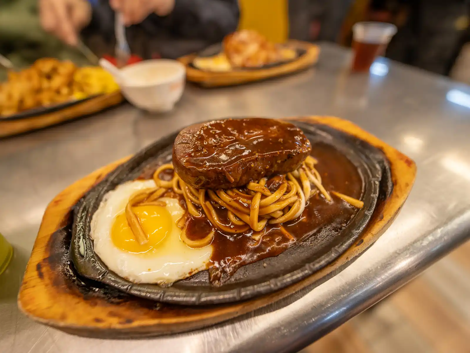 A perfectly cooked thick slab of steak smothered in sauce rests on top of a plate of noodles, ready to eat.