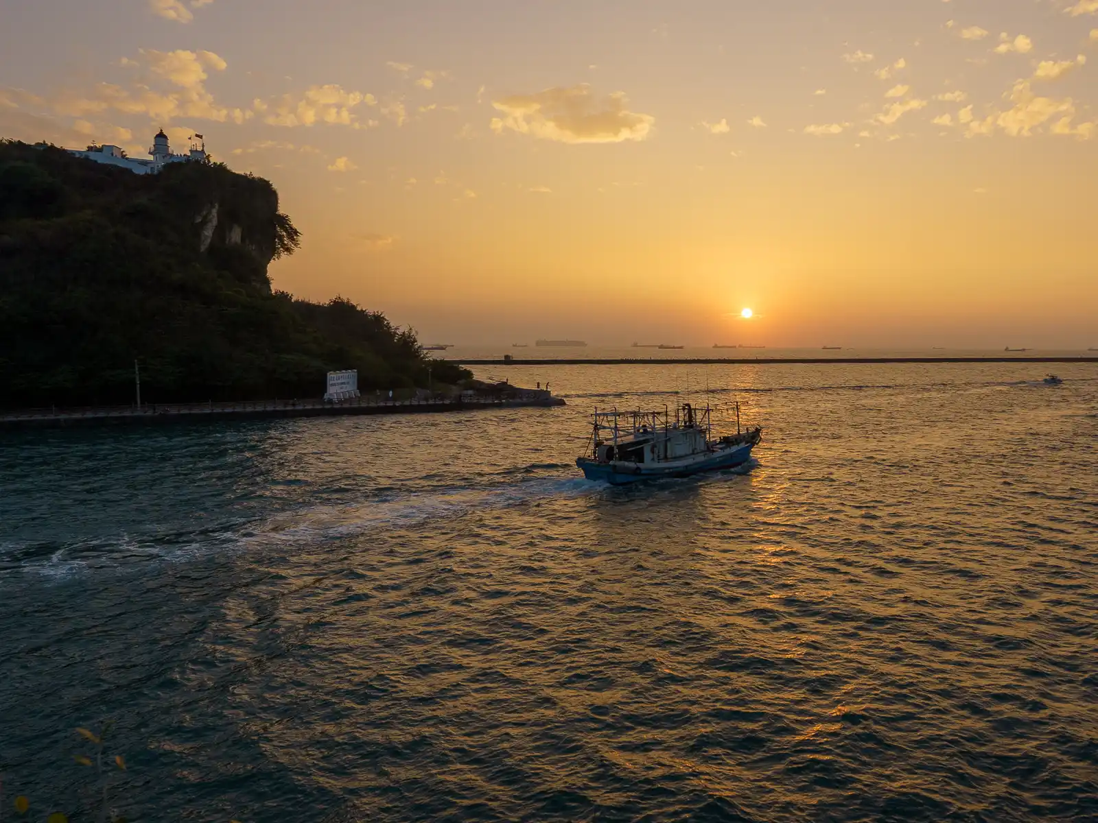 The sun sets over the horizon as a fishing boat exits the harbor.