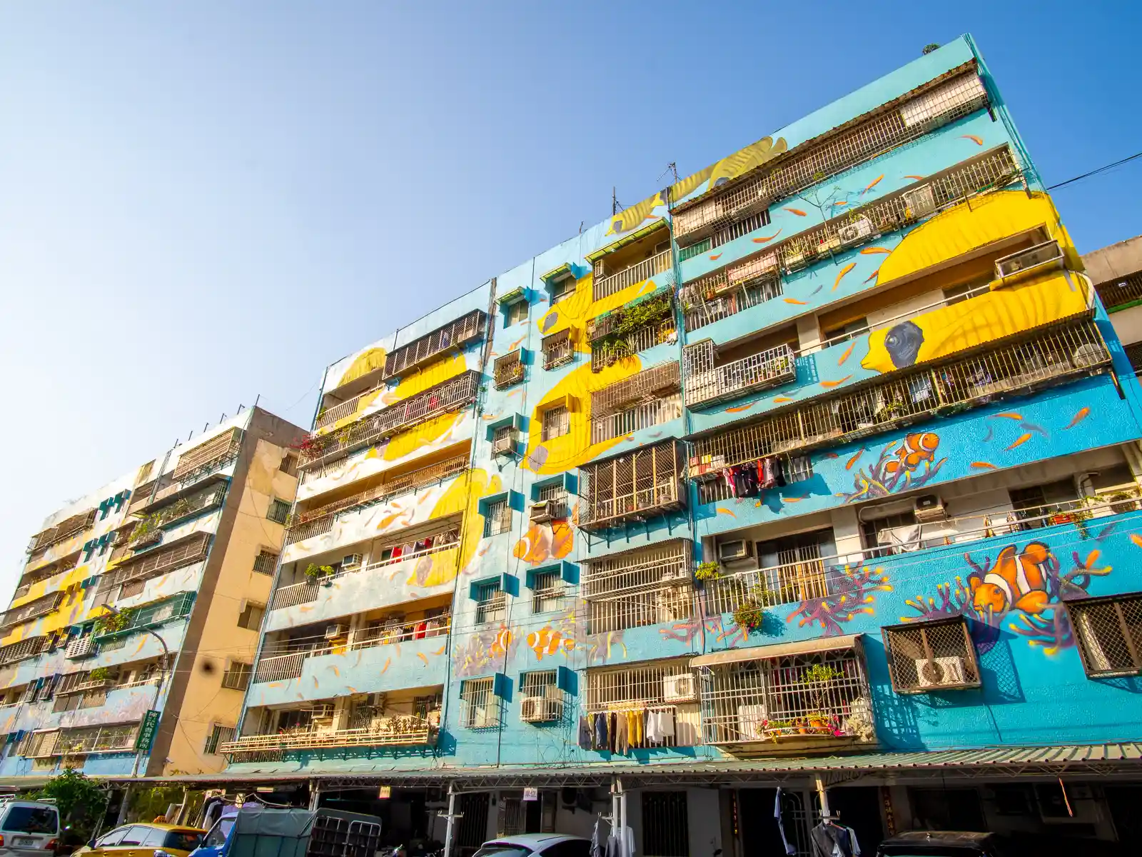 The side of an apartment building is home to a massive building-size mural featuring fish, seaweed, and coral.