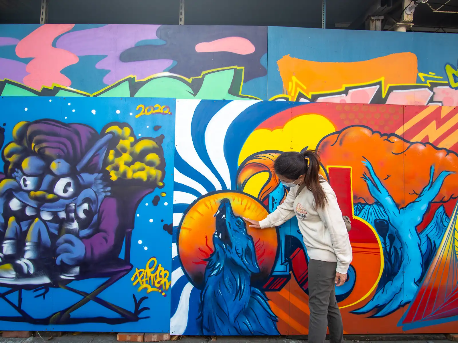 A tourist poses with a graffiti painting of a small howling wolf.