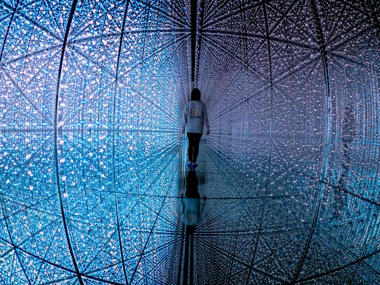 Crystal lights are mirrored to create a symmetrical space-like scene with a person at the center.