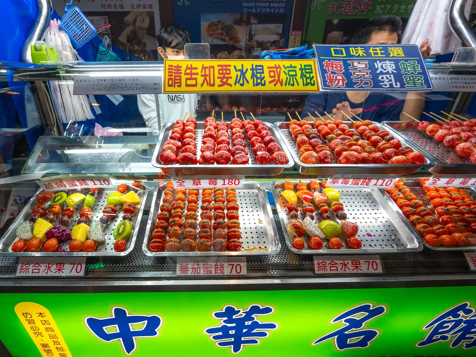 Glazed candied fruits are on display at a street food stand.