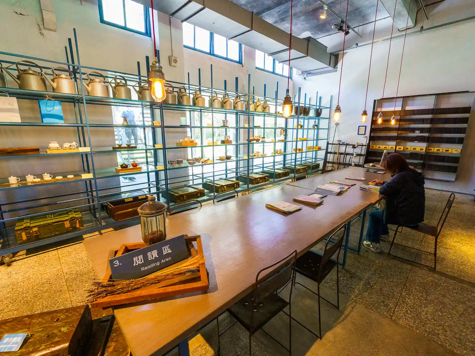 Teaware is displayed on shelves surrounding a long table in the reading area.