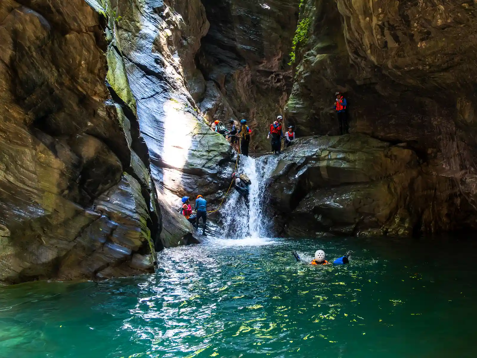 Hikers take turns climbing directly out of a deep pool, up and over a 3-meter-tall waterfall.