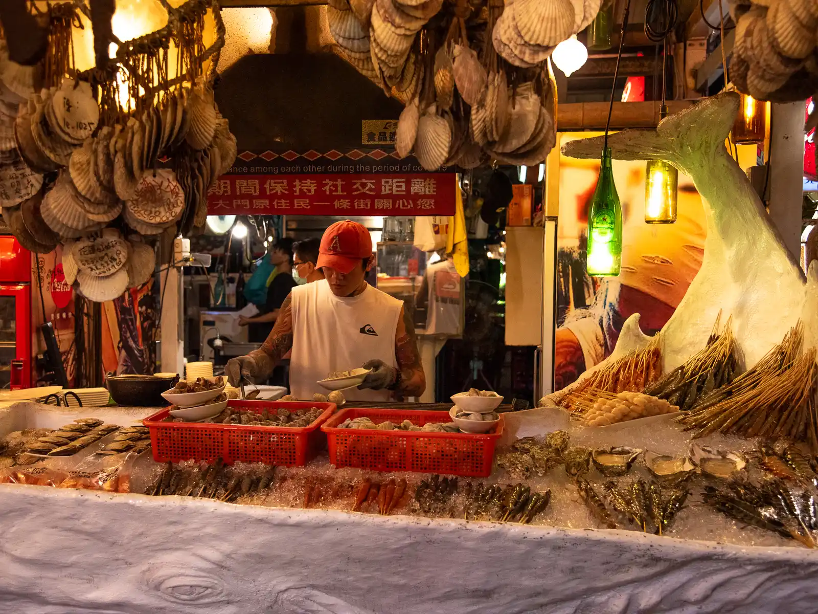 A seafood stall is decorated with hanging shells and a sculpture of a whale's tail.